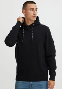 Zwarte hoodie met verstelbare trekkoorden, ribgebreide boorden en zoom. Gemaakt van zachte stof met een gestructureerde afwerking.