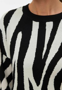 Close-up van een persoon die een zwart-witte trui met zebra-strepen en ronde hals draagt.