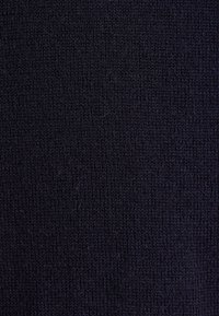 Gros plan d’un tissu bleu marine foncé étroitement tricoté avec des motifs de couture verticaux et horizontaux visibles.