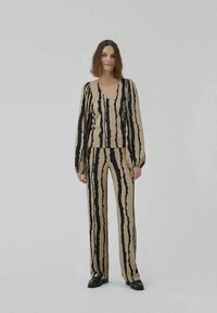 Beige outfit with black vertical stripes, featuring a V-neck blouse and wide-leg pants. Smooth texture, long sleeves, relaxed fit.