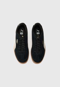 Black suede sneakers with a gum sole, featuring black laces, a white side stripe, and gold branding. Round toe design with minimal accents.