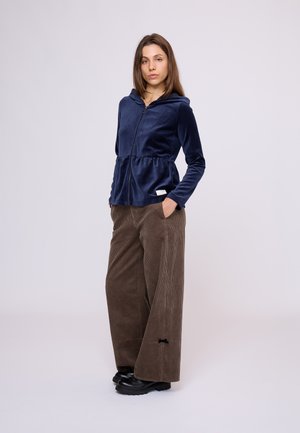 Marineblauwe fluwelen jack met rits en capuchon, peplum taille; gecombineerd met brede bruine corduroy broek met een subtiele zwarte strikdetail.