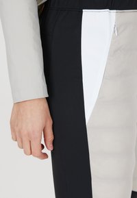 Svarta och beige träningstights med en vit detalj, featuring en dragkedjeficka och en slät yta; figurnära design med synlig midja.