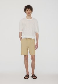 Camicetta bianca a maniche corte con texture, pantaloni corti beige con coulisse e sandali marroni. Design semplice e casual con vestibilità rilassata.