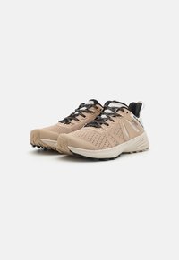 Baskets de sport beiges clairs avec accents noirs, dessus en maille texturée, col rembourré et lacets multicolores. Semelle en caoutchouc antidérapante.