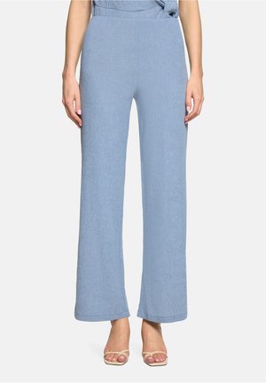 Hellblaue Hose mit weitem Bein, getragen von einer barfuß stehenden Person, Frontansicht vom Taillen- bis zum Fußbereich vor einem einfarbigen Hintergrund.