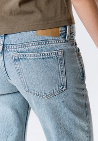 Svetlo modre kavbojke iz jeansa z zamolklo obdelavo, z obliko čistih zadnjih žepov, kontrastnim šivom in usnjenim pasnim napisom v barvi konjaka.