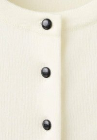 Primo piano di tessuto di maglia color crema con tre bottoni rotondi neri lucidi allineati verticalmente.