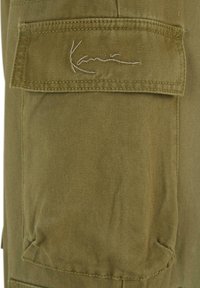 Olivgrünes Cargo-Hosentaschen mit genähten Details und gesticktem „Kane“-Logo. Besitzt eine glatte Textur und strapazierfähigen Stoff.