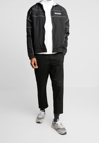 Sort lynlåsjakke med hvide detaljer, parret med en hvid turtleneck, sorte bukser og sølvgrå sneakers.