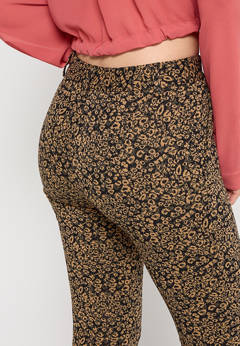 Schwarze Leggings mit einem dezenten braunen Blumenmuster, ausgestattet mit einem elastischen Bund und einem figurbetonten Design, kombiniert mit einem kurzen pinken Oberteil.