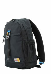 Mochila de tela negra con respaldo acolchado, correas ajustables, bolsillo frontal y bolsillo de malla lateral. Presenta herrajes azules y un parche con el logo.