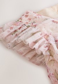 Pink blomsterstof med lagdelte flæser lavet af tyndt tyl, der viser en sart tekstur og bløde pastelfarver på en lys baggrund.