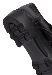 Zwarte schoen met een ronde neus, een gestructureerde rubberen zool, gedetailleerde brogue-accenten en een gladleren bovenkant. Het ontwerp heeft een laag uitgesneden profiel.