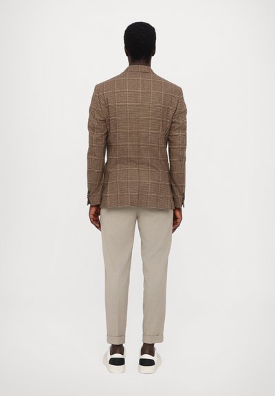 Brown plaid blazer with structured design, paired with light beige trousers and white sneakers with black accents, viewed from the back.