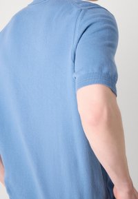 Polo bleu clair à manches courtes avec un col en maille texturée et des poignets côtelés, présentant une finition en tissu lisse et une coupe ajustée.