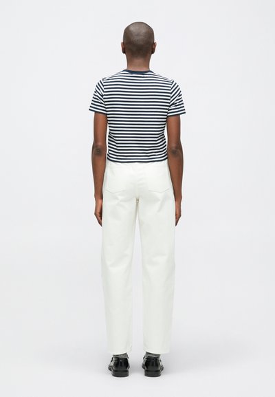 Prúžkovaný námornícky a biely top s krátkym rukávom a skráteným strihom, skombinovaný s bielymi nohavicami s vysokým pásom a čiernymi topánkami, z pohľadu zozadu.