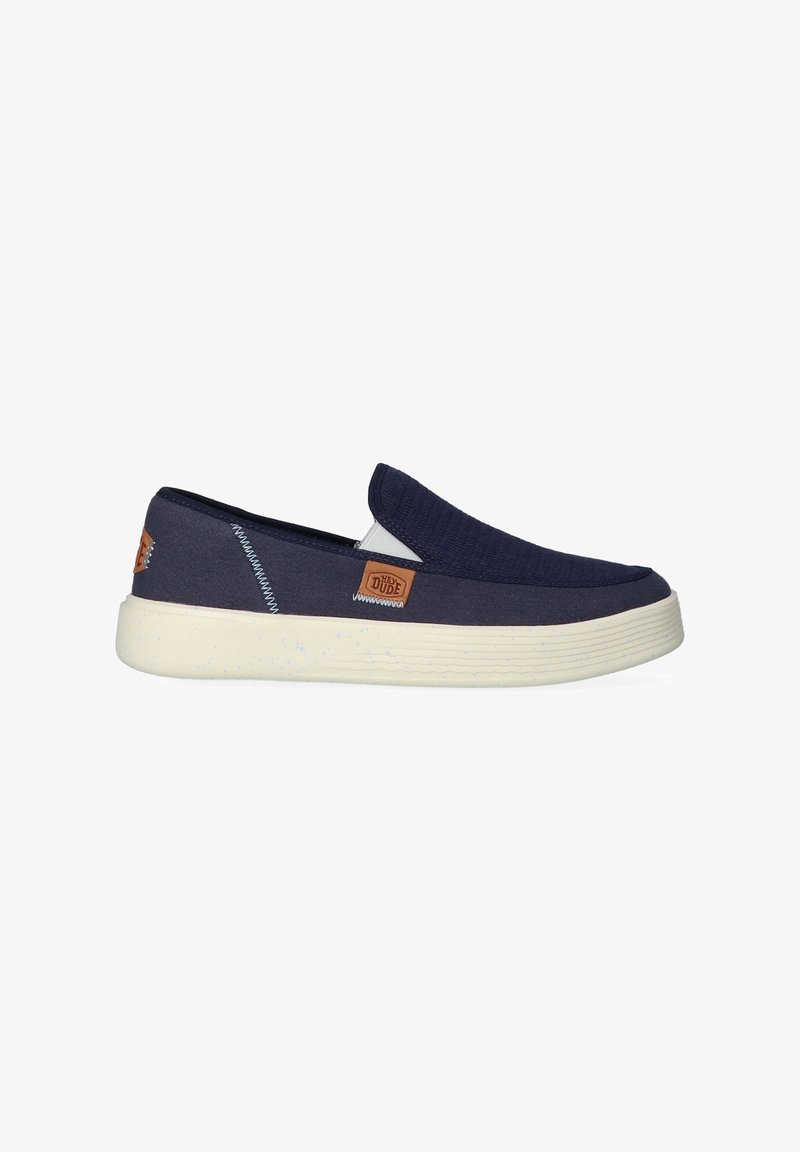Marine slip-on schoenen met een gestructureerde bovenkant, een licht gevlekte zool en tan logo-accenten aan de zijkant. Eenvoudig, casual ontwerp.