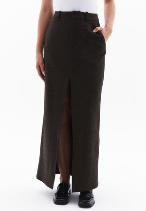 Long brown skirt with a front slit, made of textured fabric. Features side pockets and a fitted waist. Paired with black shoes.