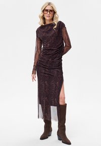 Sukienka z długim rękawem z brązowym nadrukiem w wężowy wzór, marszczonymi detalami, bocznym rozcięciem i półprzezroczystymi rękawami, zestawiona z brązowymi kozakami za kolano.