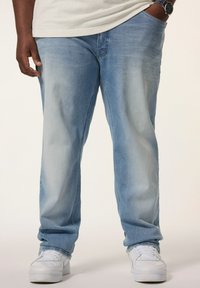 Vaqueros azul claro con una textura desgastada, diseño de pierna recta y estilo de cinco bolsillos, combinados con zapatillas blancas.
