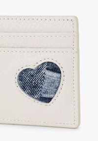 Portafoglio in pelle bianca con una toppa in denim a forma di cuore. Presenta più slot per carte e dettagli di cucitura in contrasto.