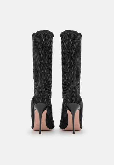 Black, knee-high heeled boots featuring a textured fabric with rhinestone accents, pointed toe, and stiletto heel design.