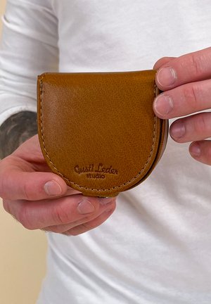 Brązowy skórzany portfel na karty o zaokrąglonym kształcie, z teksturowaną powierzchnią, zszytymi brzegami oraz wytłoczonym logo "Gusti Leder studio".