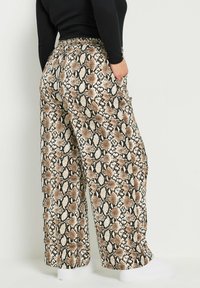 Yksinkertaiset leveälahkeiset housut käärmeennahkakuviolla, jossa sekoitus ruskeaa, beigeä ja mustaa. Varustettu joustovyötäröllä ja sivutaskuilla. Pehmeä, teksturoidusta kankaasta valmistettu.