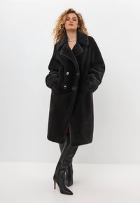 Schwarzer Kunstpelz-Doppelreiher-Mantel mit großem Kragen und Vordertaschen. Verfügt über sechs Knöpfe und eine lockere Passform, die bis zur Mitte des Oberschenkels reicht.