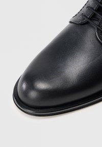 Scarpa in pelle nera con punta arrotondata, texture liscia e leggero lucido. I lacci e i dettagli di cucitura sulla parte superiore arricchiscono il design.