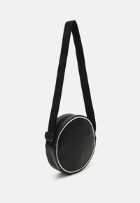 Borsa circolare nera realizzata in pelle sintetica testurizzata. Presenta un bordo bianco e una tracolla in tessuto regolabile. Chiusura con cerniera nella parte superiore.