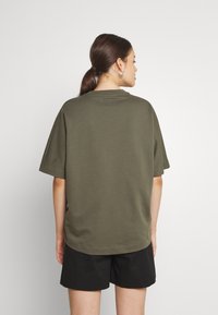 T-shirt in cotone verde oliva con maniche corte e vestibilità rilassata, caratterizzato da un colletto rotondo e una texture liscia.