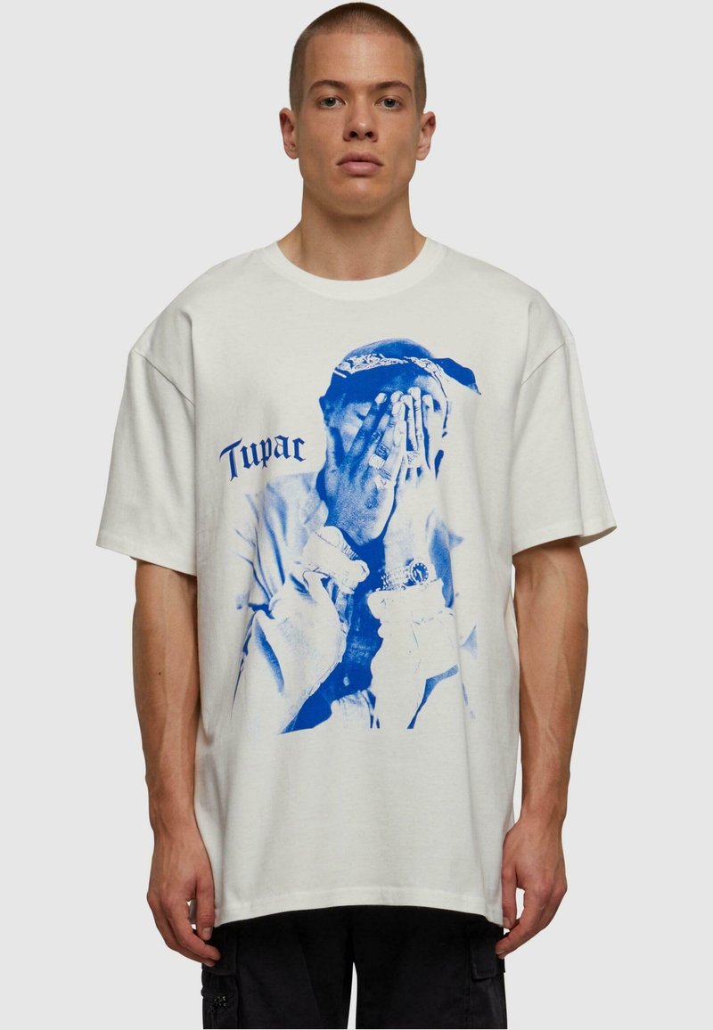 Bomulds T-shirt i off-white med en blå grafik, der forestiller en figur, der dækker sit ansigt. Har korte ærmer og en afslappet pasform.