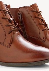 Bottines en cuir marron à finition lisse, bout arrondi, lacets sur le devant et fermeture éclair latérale. Présentent des détails de couture subtils.