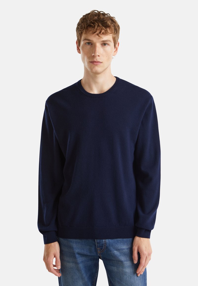 Navyblauer Rundhalsausschnitt-Pullover aus weichem Material mit langen Ärmeln und gerippten Bündchen. Über blauen Denim-Jeans getragen.