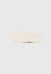 Weiße Sneaker-Sohle mit strukturiertem Gummi und eingeprägtem "EXCHANGE"-Schriftzug, entworfen für Grip und Langlebigkeit. Einfache, glatte Kanten.
