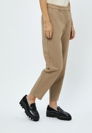 Tan tapered trousers with a smooth texture, featuring a flat front and side pockets, paired with black chunky loafers.