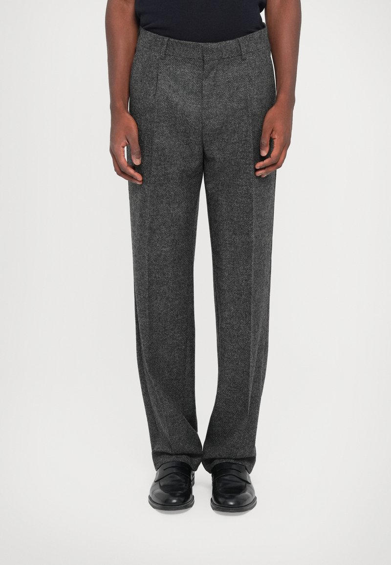 Grå skræddersyede bukser med et tekstureret herringbone-mønster. Straight-leg design med en frontfolder og bæltesløjfer. Båret med sorte sko.