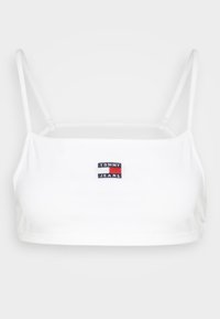 Bílá krátká tílko s tenkými ramínky, na kterém je vpředu vyšívané logo "TOMMY JEANS" v modré, červené a bílé barvě. Hladký textilní povrch.