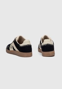 Sneaker neri e crema con superiore in tessuto testurizzato, suola in gomma e dettagli cuciti sul tallone; design a bassa altezza.