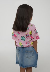 T-shirt di cotone rosa con stampe colorate di gelato, ciambella e fiori, abbinata a una gonna di jeans con due tasche posteriori.