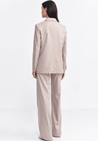 Beżowy garnitur w paski, dopasowany krój, marynarka z klapami typu notch, spodnie szerokie, gładki materiał, trzypunktowy detal na rękawach, minimalistyczny styl.