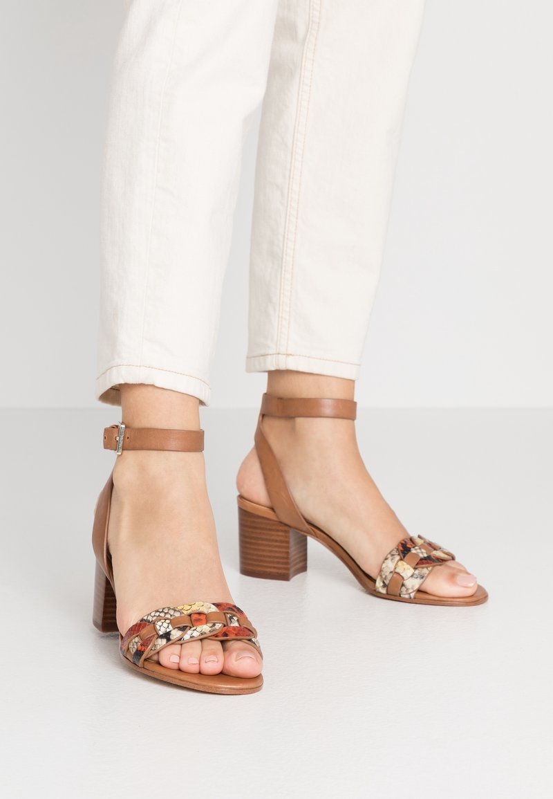 Sandales à talons en cuir marron avec une tige tressée à motifs multiples et une bride à la cheville, dotées d'un talon épais et texturé.
