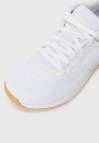 White athletic shoe with a mesh upper, textured finish, and a rubber sole. Features laces and a muted Reebok logo on the side.