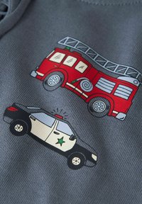 Tessuto grigio con grafiche di un camion dei pompieri rosso e un'auto della polizia in bianco e nero. I disegni includono dettagli come ruote, finestre e una scala.