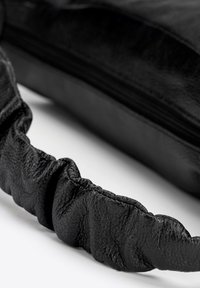 Czarna skórzana torba z teksturowanym, marszczonym paskiem oraz zamknięciem na zamek. Powierzchnia posiada gładkie wykończenie i delikatne detale tekstury.