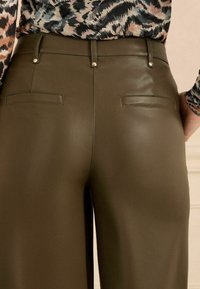 Augstās jostasvietas olīvu zaļās mākslīgās ādas bikses ir ar elegantu dizainu, divām aizmugurējām kabatām un metāla akcentiem uz jostasvietas papildu detaļām.