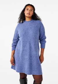 Vestido de punto en azul claro con textura acanalada, mangas largas y patrón geométrico. La forma en A se extiende hasta la mitad del muslo.