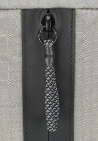 Tela tejida gris con acentos sintéticos negros, con un tirador de cremallera que incluye un cordón trenzado texturizado en blanco y negro y un anillo de metal.